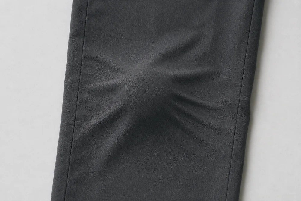 A close crop of the knee of trousers lying flat, showing a soft rounded bulge.